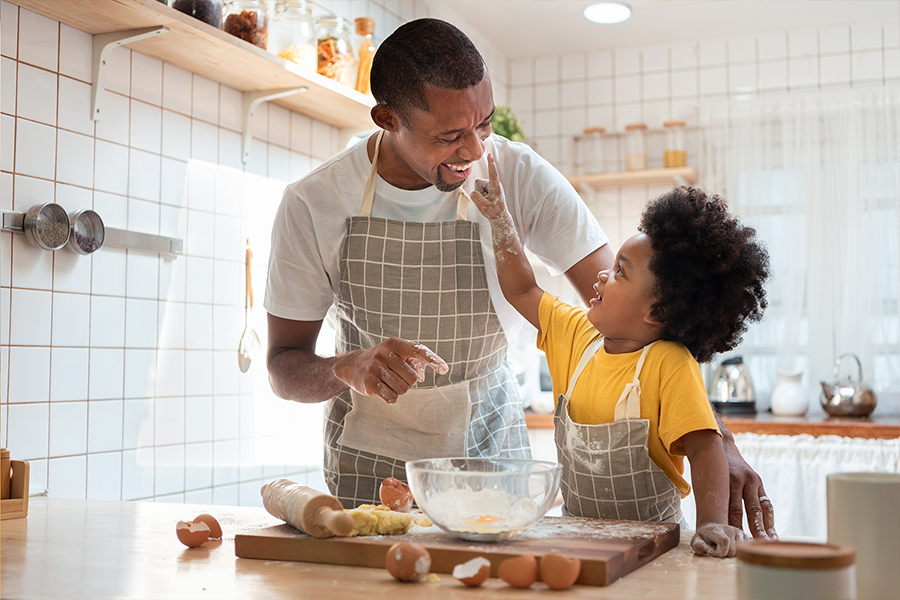 Black father and son having fun while baking cookies at home together.