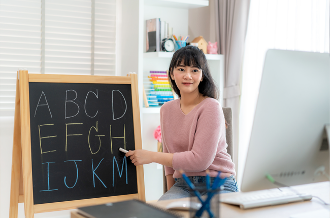 Asian woman teacher teaching English alphabet on chalkboard from her home via video conference