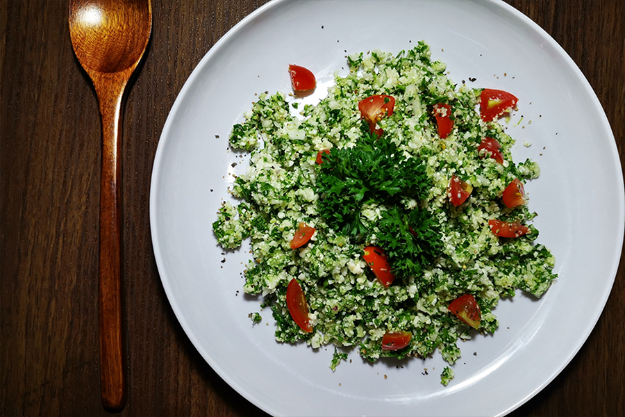 Plate of Cauliflower Tabbouleh Salad and tomatoes with a wooden spoon next to the plate