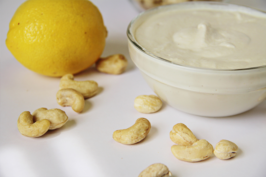 Sauce bowl of cashew cream sauce with scattered cashews arond the bowl and lemon