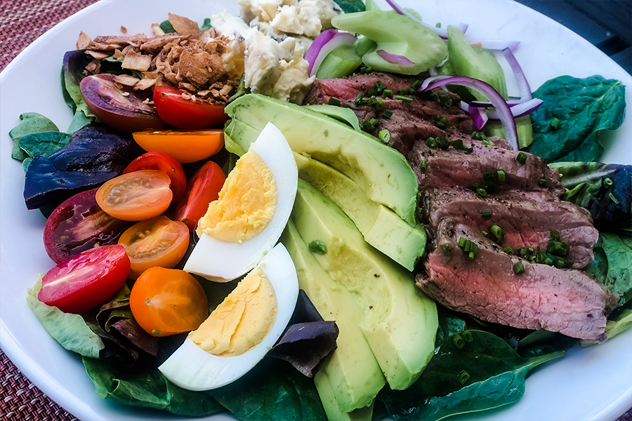 Cobb salad with tomatoes, hard boiled eggs, flank steak, avocado and other toppings