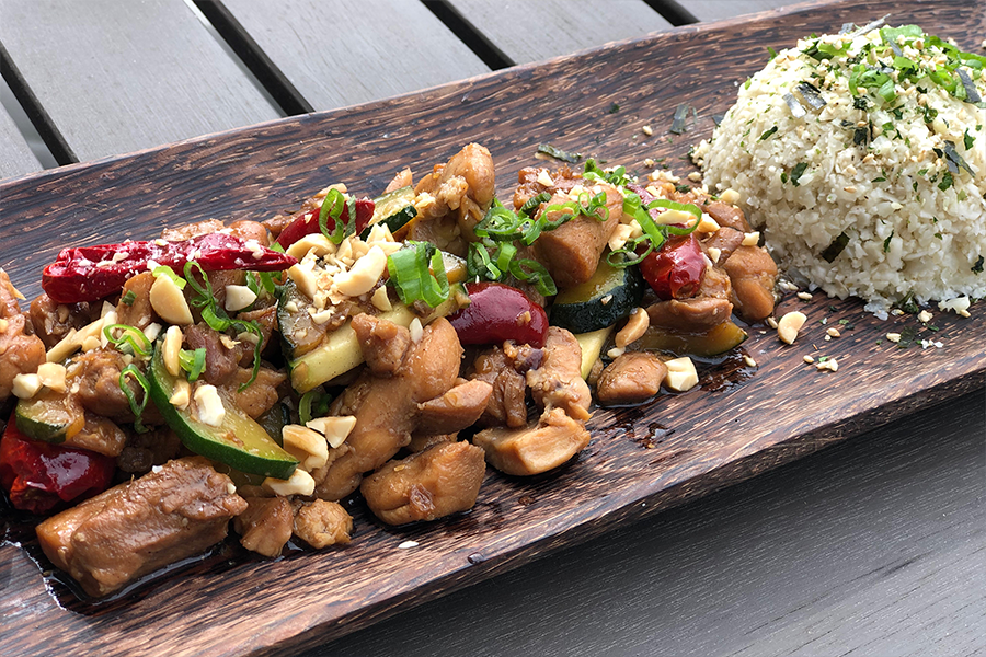 Kung Pao Chicken plated on a long wooden plate with a mound of rice