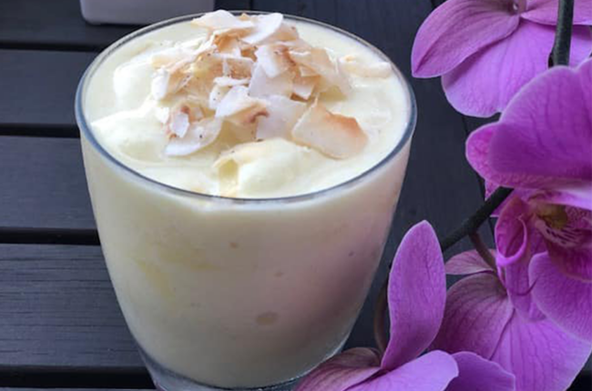 Pineapple-Toasted Coconut Smoothie in a glass next to purple orchids