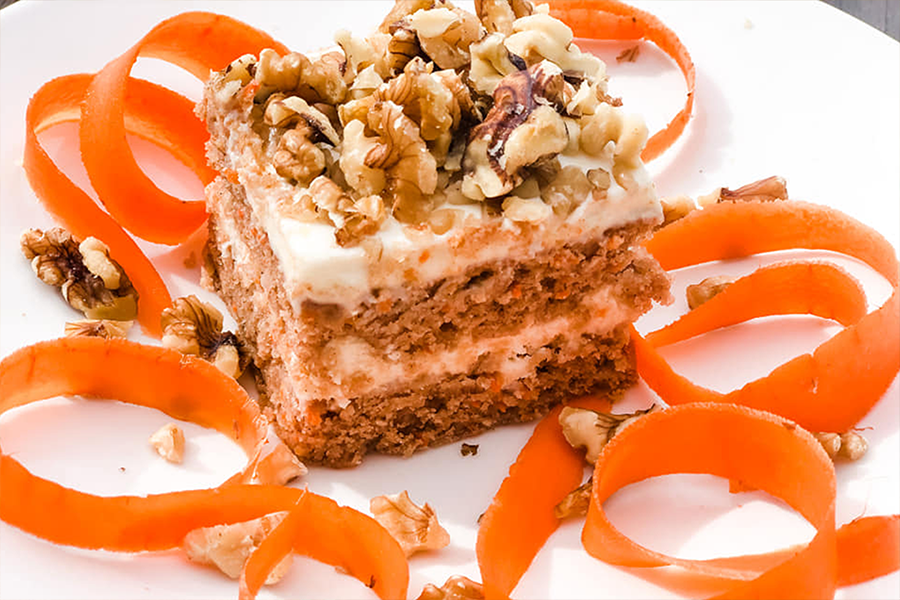 Square piece of Vegan Carrot Cake topped with almonds on a plate decorated with carrot ribbons