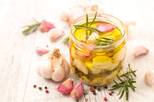 Small jar of olive oil infused with garlic cloves and rosemary