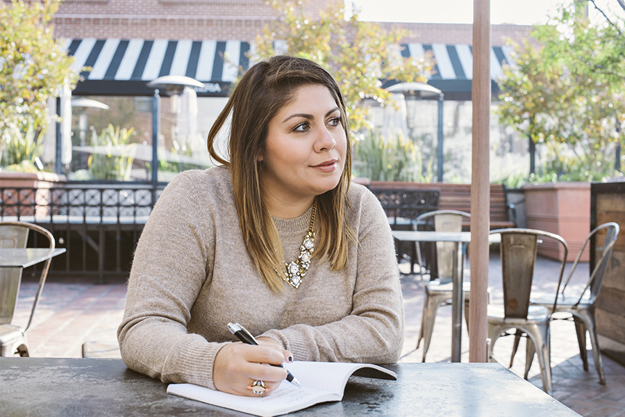 A young latina woman sits at a cafe with a journal, thinking about her goals for the coming year