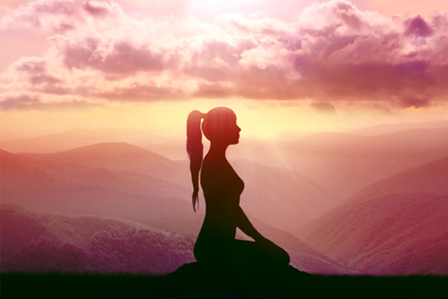 Silhouette of a woman kneeling with mountains and the sunset behind her