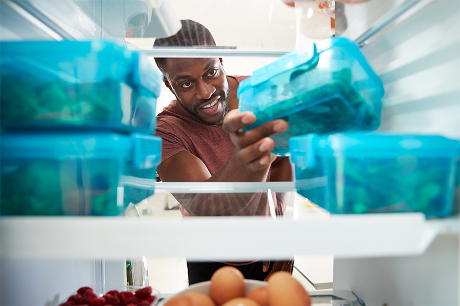 View looking out from inside of refrigerator as a Black man takes out healthy packed lunch in container
