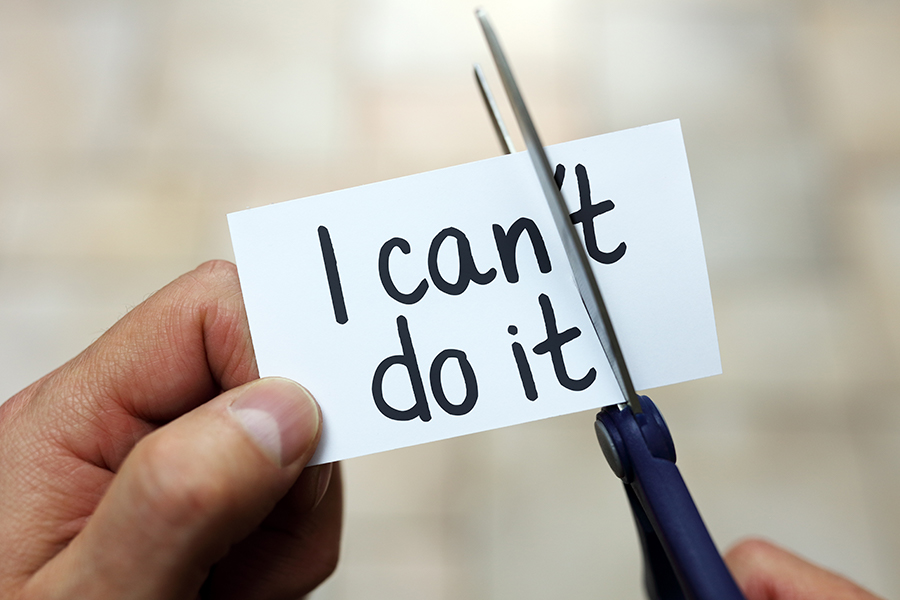 Hand holding a piece of paper that says "I can't do it" with scissors cutting off the "'t" so it say "I can do it"
