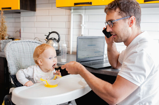 Dad working, on the phone, while feeding his baby