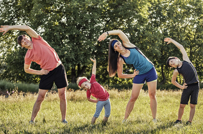 Mom, dad and 2 young boys outside stretching in workout clothes