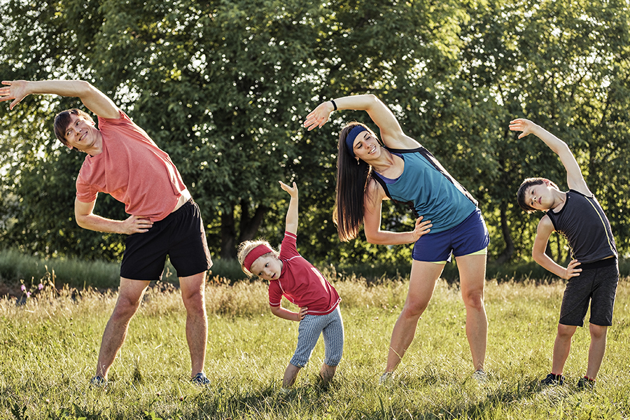 Mom, dad and 2 young boys outside stretching in workout clothes