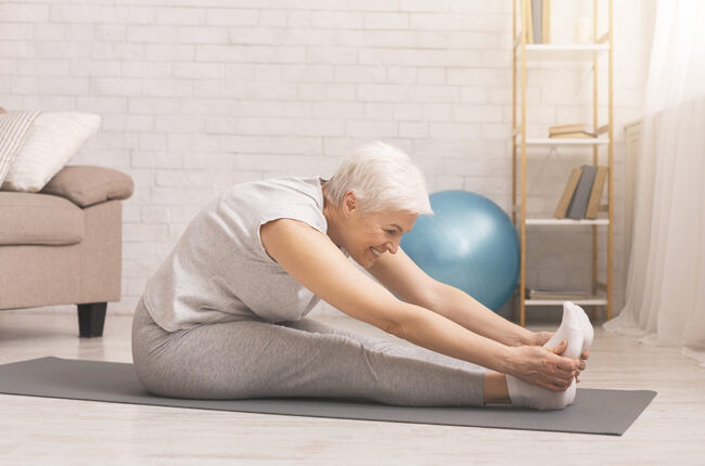Eldery woman sitting on yoga mat reaching for her toes stretching