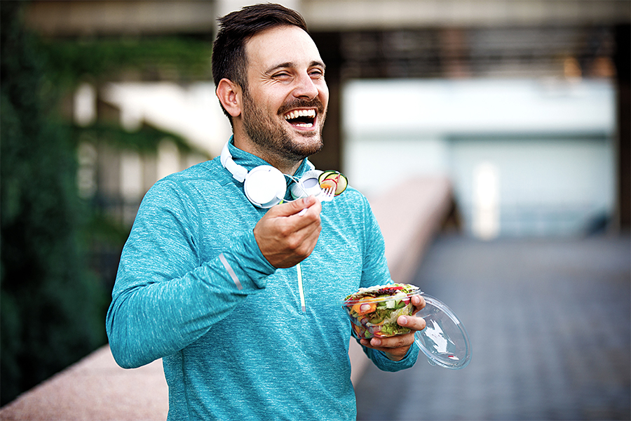 Man in workout clothes outside eating a salad and smiling
