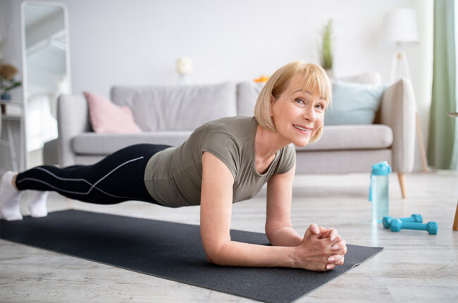 Smiling senior woman doing elbow plank on yoga mat in living room