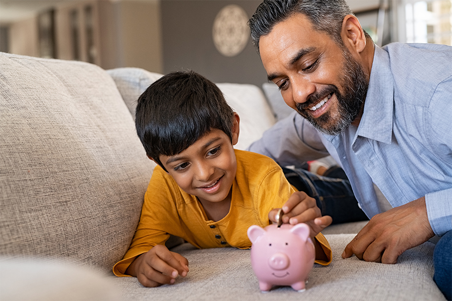 Indian father teaching son about money, putting money in piggy bank