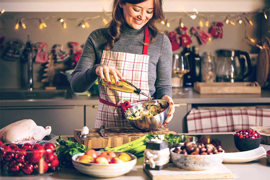 Woman pouring olive oil on a salad in a winter/holiday themed kitchen