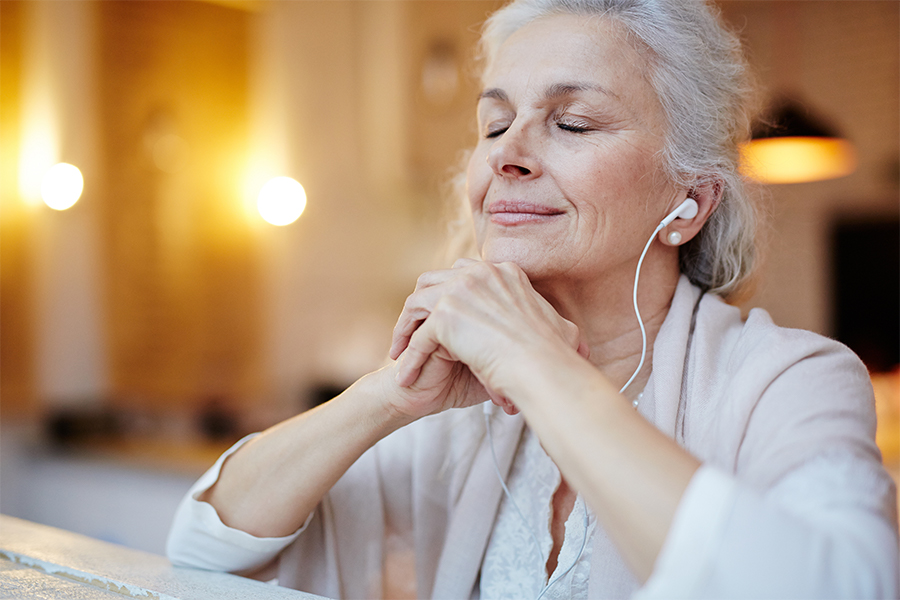 Older woman eyes closed listening to earphones, resting head on hands