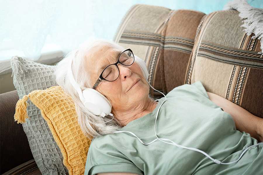 Elderly woman lying on couch with headphones on