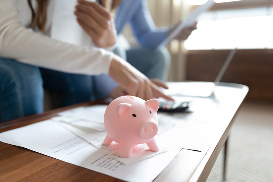 Close up focus on little pink piggybank on table. Young family couple managing financial monthly budget, calculating expenses or savings investment, paying bills together indoors, money concept.