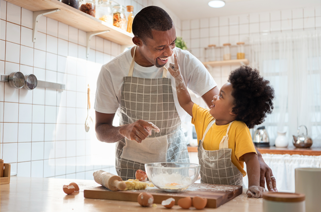 Black father and son having fun while baking cookies at home together.
