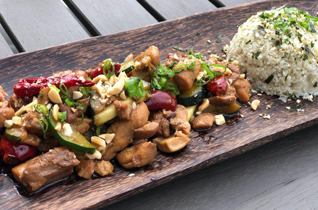 Kung Pao Chicken plated on a long wooden plate with a mound of rice