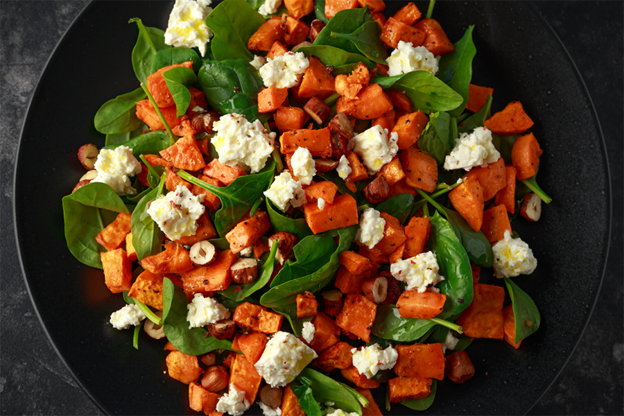 Healthy roasted sweet potato salad with spinach, feta cheese, and nuts on a black plate