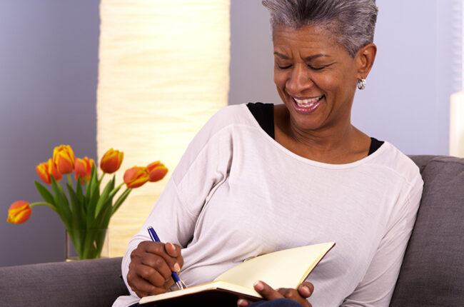 Senior black woman writing in journal on the couch