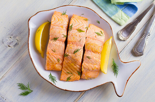 Fish-shaped bowl with 3 poached salmon filets and lemon slices