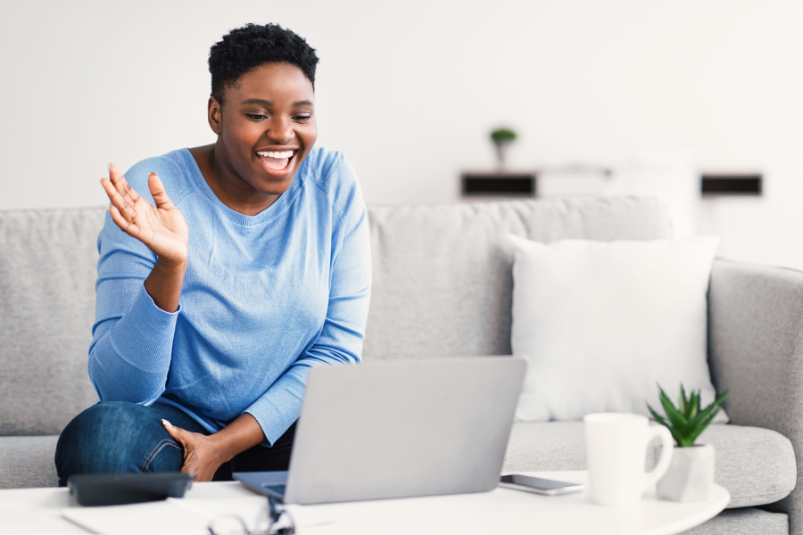 Black woman sitting on couch waving hello to someone on zoom