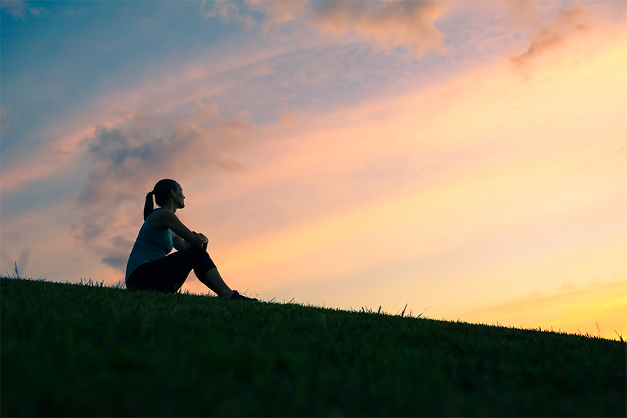 Woman sitting on hill at sunset thinking
