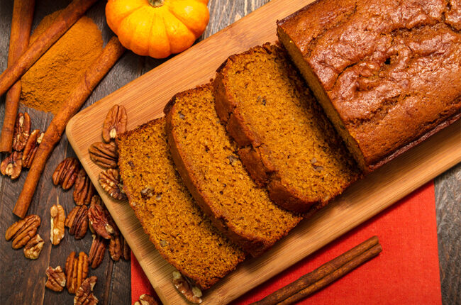 Pumpking bread slices and loaf on a cutting board with walnuts scattered around