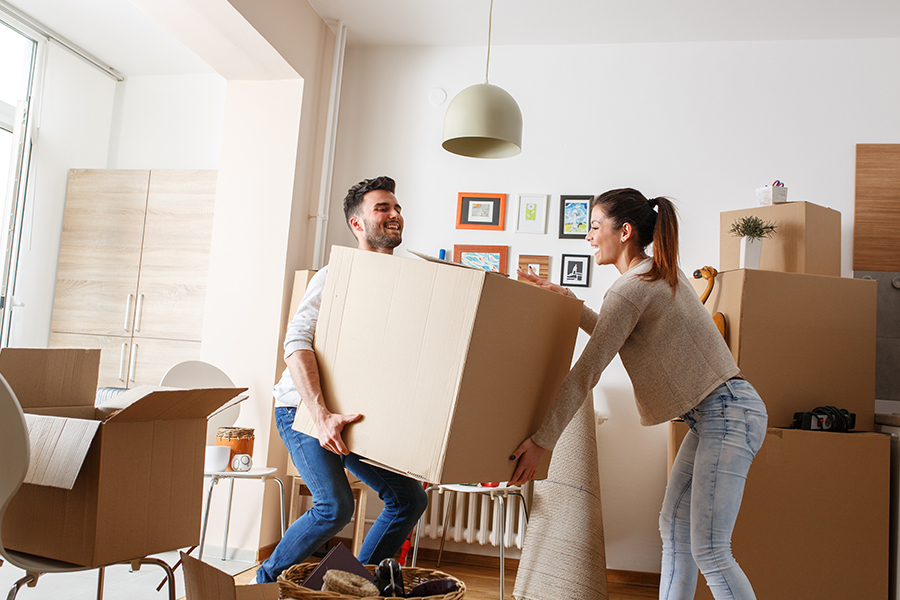 Young couple carrying big, heavy box moving into new home