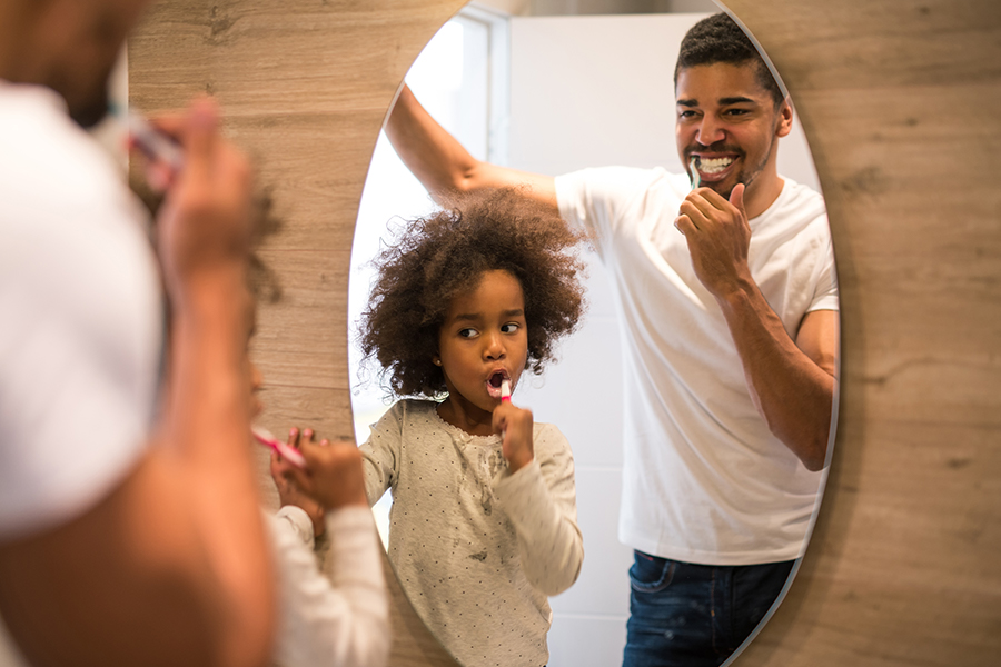 Black father and little girl brushing teeth together