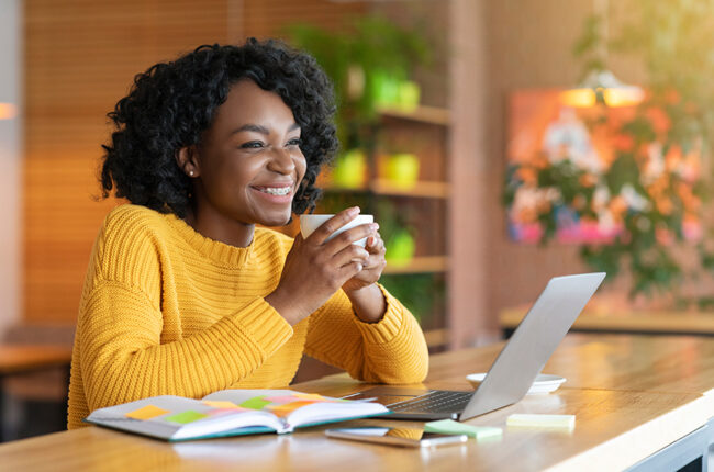Happy, smiling black woman enjoying coffee at her desk