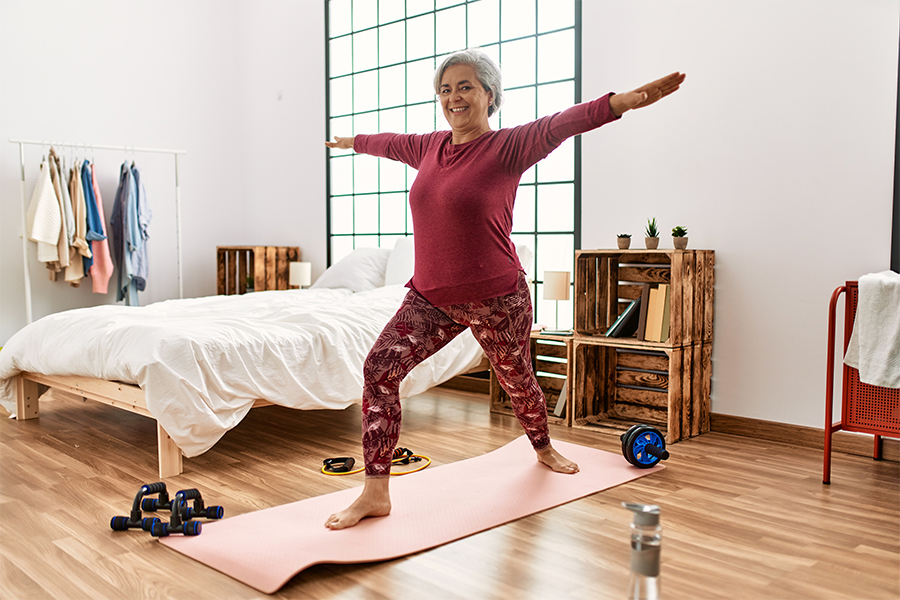 Middle age grey-haired woman training yoga at bedroom.