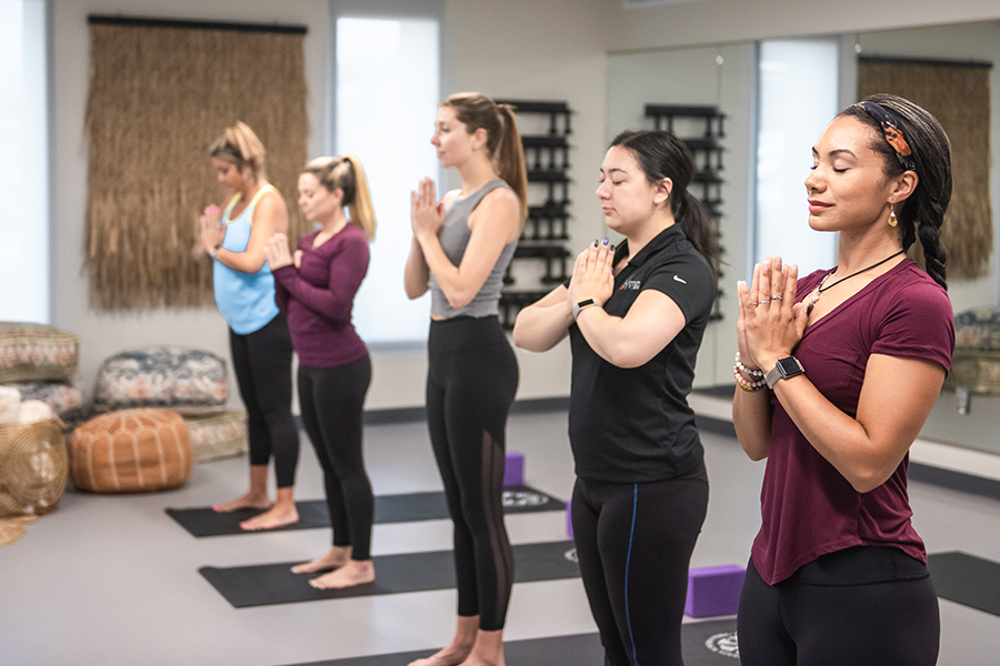 5 women in a yoga studio, standing with hands pressed together at heart center