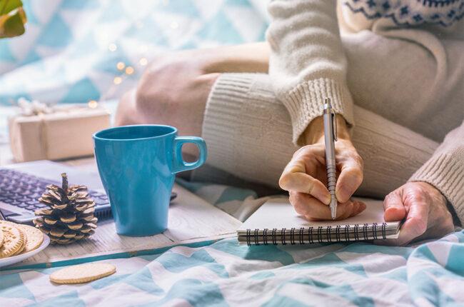 Close up of woman writing in a notebook on her bed, cozy winter holiday morning