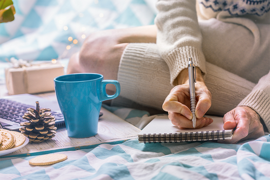Close up of woman writing in a notebook on her bed, cozy winter holiday morning