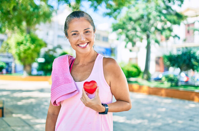 middle-aged woman outside in exercise clothes holding a heart stress ball