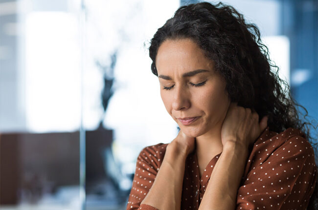 Hispanic woman overtired working in modern office businesswoman has severe neck pain, massages neck muscles, business woman in casual clothes and curly