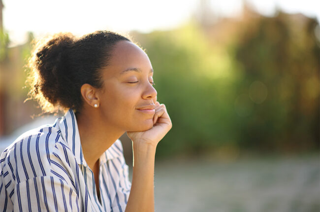 Relaxed Black woman resting in a park, eyes closed, head in palm