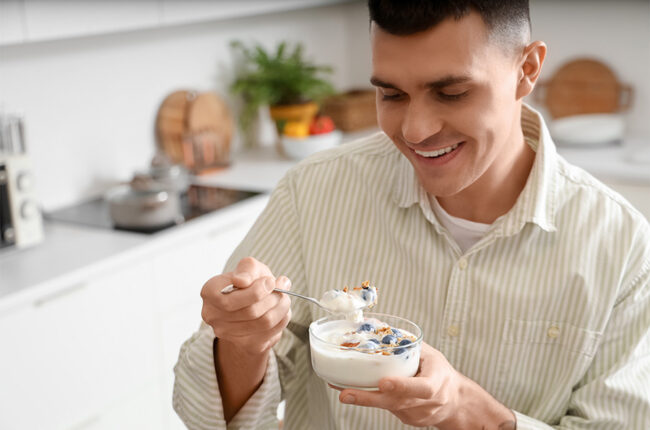 Young man with tasty yogurt in kitchen, closeup