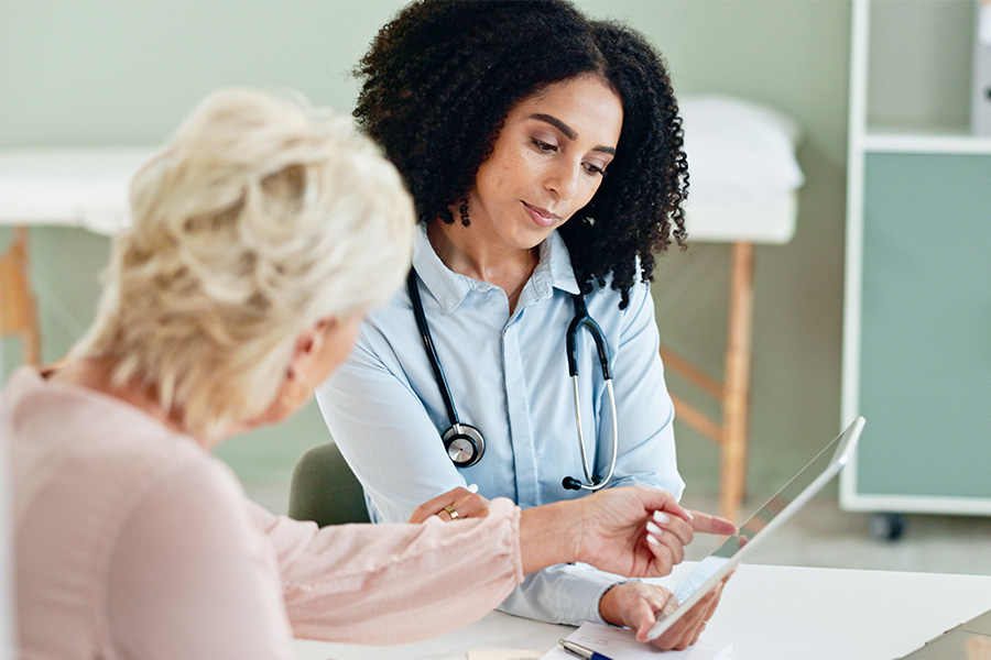 Elderly woman and young female doctor looking at an iPad reviewing health insurance information in a medical office